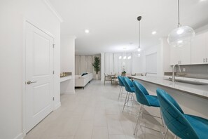 Eine moderne Küche mit weißen Schränken, einer Edelstahl-Arbeitsfläche und blauen Barhocker.