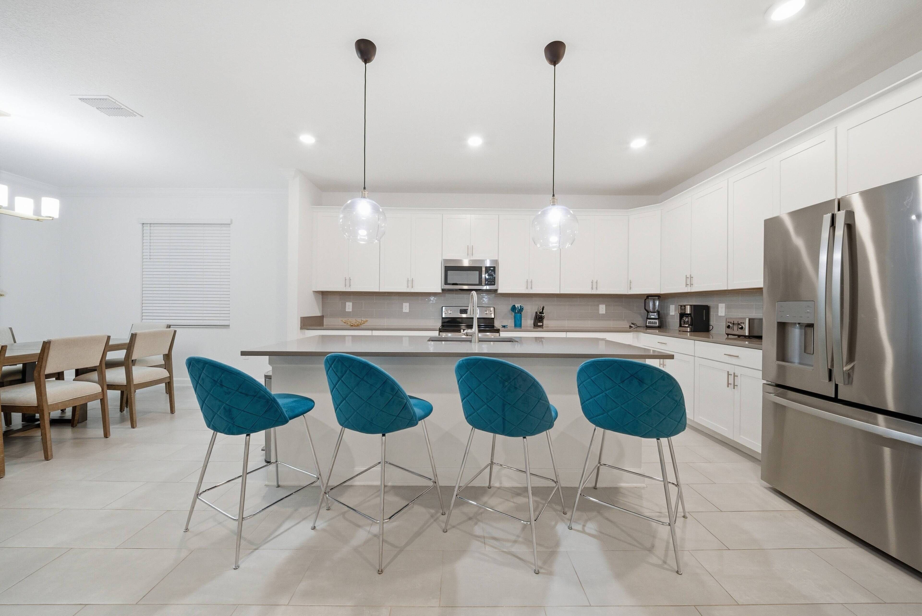 Una cocina moderna con gabinetes blancos, electrodomésticos de acero inoxidable y taburetes de bar azules.