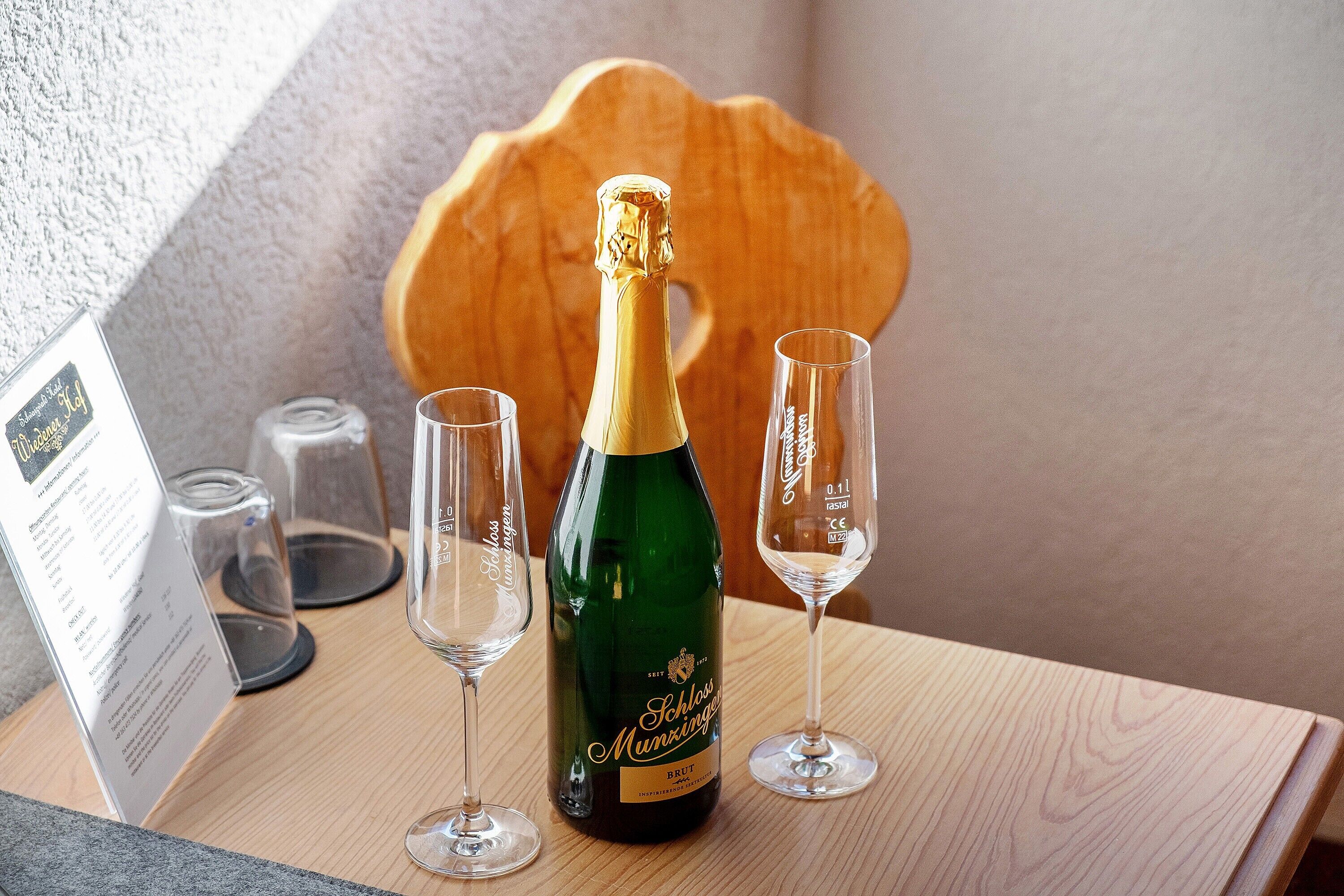 A bottle of Schlosser Munzingen Brut wine, two glasses, and a menu on a wooden table.