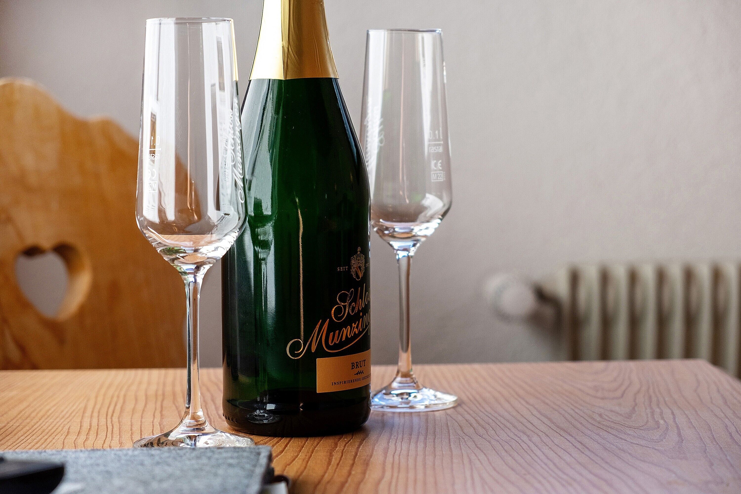 A bottle of Schlosser Munzinger Brut wine with two empty glasses on a wooden table.
