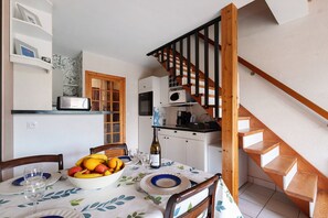 A dining area with a table set for two, a bowl of fruit, and a bottle of wine. - “Le Cormoran” Apartment with South-Facing Balcony, Steps from the Harbor (Pornic)