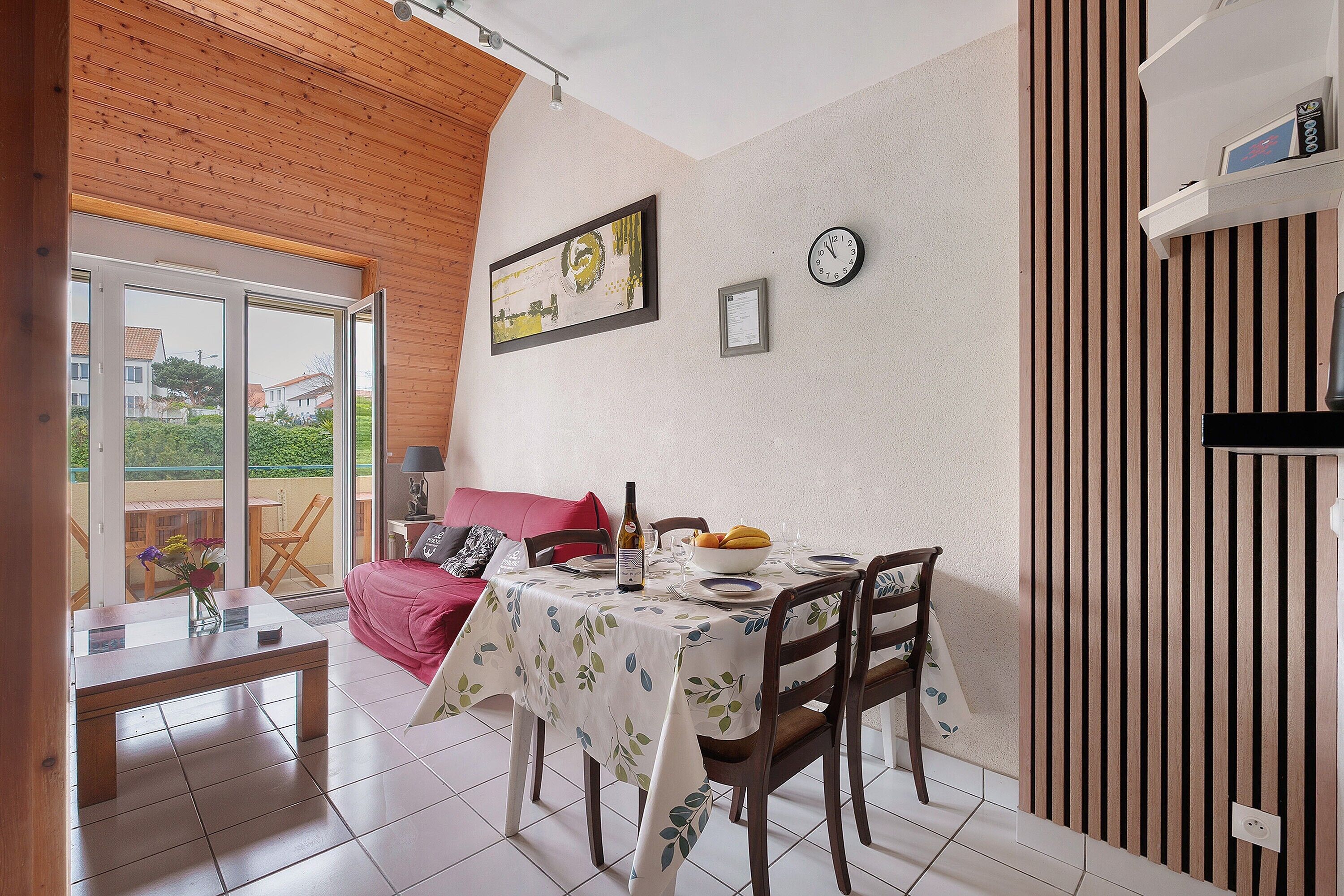A dining area with a table set for two, a clock, and a framed picture on the wall.