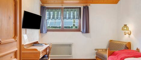 A room with a wooden desk, a bed, a radiator, and a window with curtains.