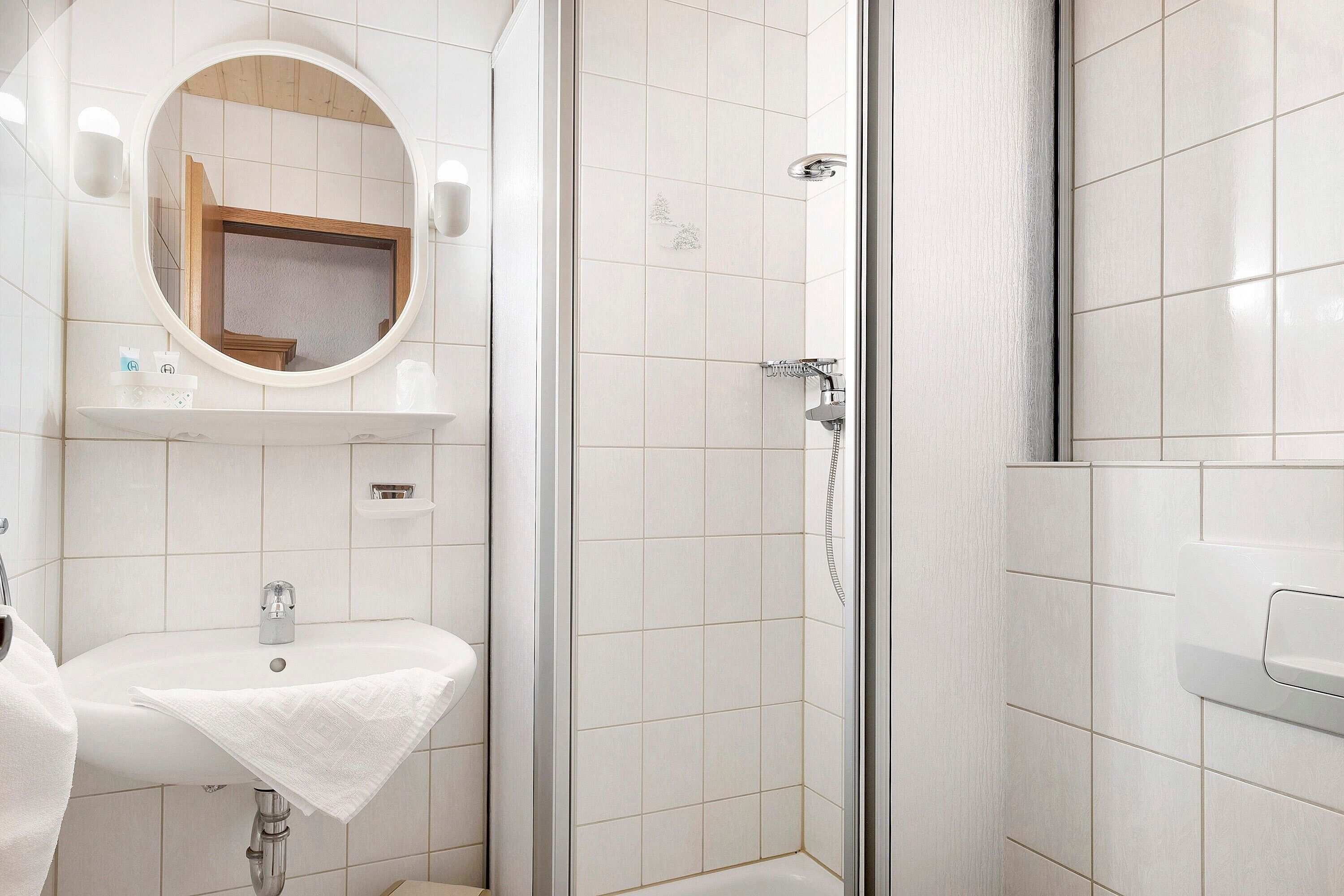 A bathroom with a sink, mirror, shower, and tiled walls.