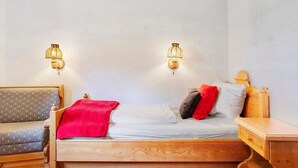 Ein hölzernes Bett mit roter Decke, zwei Kissen und einem Nachttisch.