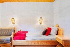 Ein hölzernes Bett mit roter Decke, zwei Kissen und einem Nachttisch.