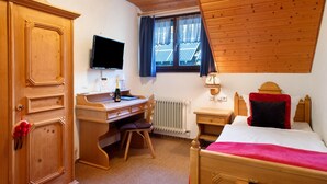 Une pièce comprenant un bureau en bois, un lit, une télévision et une fenêtre avec des rideaux.