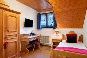 A room with a wooden desk, a bed, a television, and a window with curtains. - Room 'Einzelzimmer Standard 26' with Mountain View and Wi-Fi (Wieden)