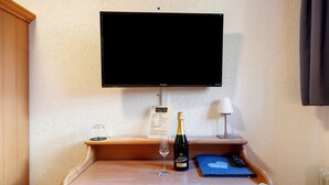Un bureau en bois, une bouteille de champagne, un verre, une télécommande et un téléviseur fixé au mur.