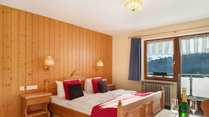 A wooden-paneled room with a bed, bedside lamps, a table with a bottle and glasses, and a window with a view. - Apartment 'Doppelzimmer Superieur 13' with Mountain View, Balcony and Wi-Fi (Wieden)