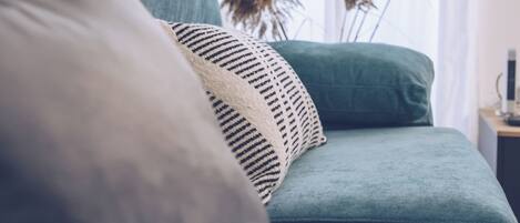 A teal sofa with a patterned pillow, a vase with dried plants, and a small table with a lamp.