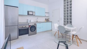 Eine moderne Küche mit einem Edelstahlkühlschrank, einer Mikrowelle, einer Waschmaschine und einem Essbereich mit einem Glastisch und Stühlen.