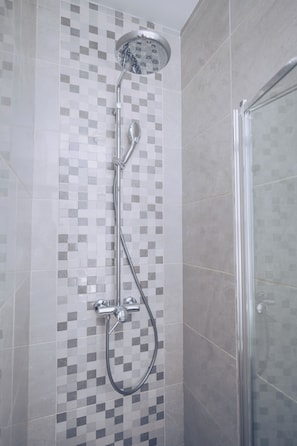 Una doccia con parete rivestita in piastrelle e porta in vetro.