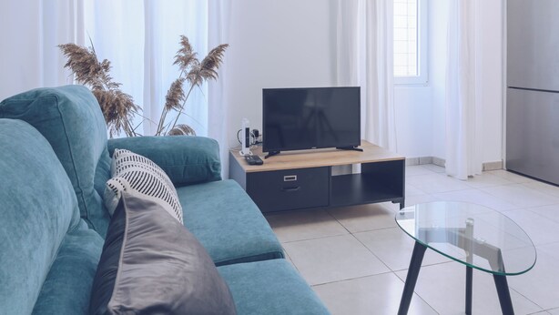 Ein modernes Wohnzimmer mit einem türkisfarbenen Sofa, einem Glastisch und einem Flachbildfernseher auf einem Holzständer.