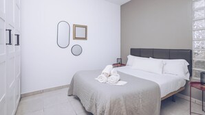 Ein Schlafzimmer mit einem Bett, einem Nachttisch, einem an der Wand befestigten Spiegel und einem Handtuchhalter.