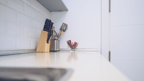 Eine Küchenarbeitsplatte mit einem Messerblock, einer Metallschale für Besteck und einem Glasgefäß.