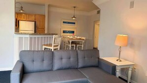 A modern living room with a grey sofa, wooden cabinets, a dining table with chairs, and a small white table with a lamp. - Runaway Beach Club 1 Bd Villa (LRW 17101) (Kissimmee)