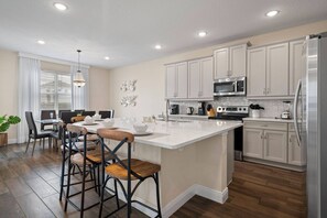 A modern kitchen with white cabinets, stainless steel appliances, and a central island with stools. - Encore Resort 5 Bedroom Home with Pool (2514) (Kissimmee)