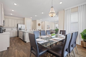 A modern kitchen with white cabinets, a stainless steel refrigerator, and a dining area with a glass table and black chairs. - Encore Resort 5 Bedroom Home with Pool (2514) (Kissimmee)