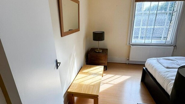 Une chambre à coucher avec un lit, une table de chevet avec une lampe, une fenêtre avec des stores et une porte.
