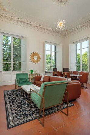 Un salon spacieux avec une grande fenêtre, un fauteuil vert, un canapé marron et un coin repas avec des chaises orange.