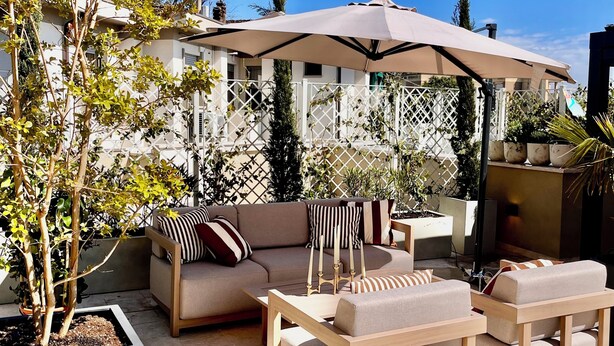 Eine Außenveranda mit einer Couch, Stühlen, einem Tisch und einem Sonnenschirm.