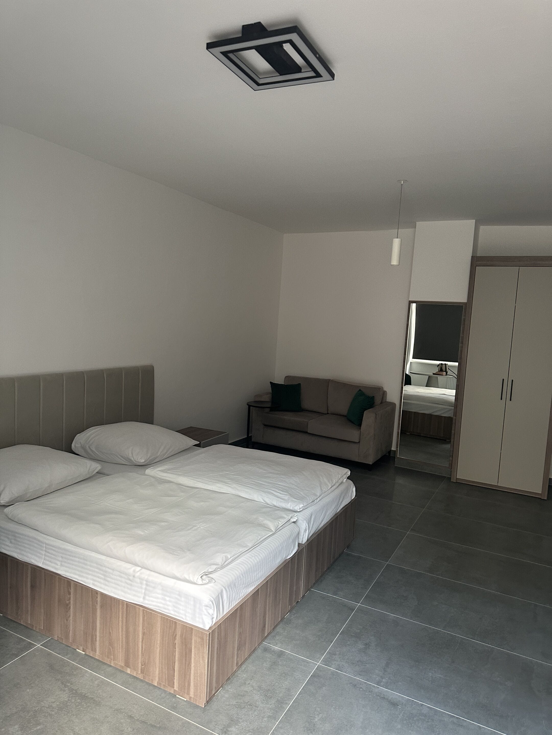 Quarto moderno com cama, sofá, guarda-roupa e espelho.