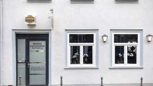 A hotel facade with a sign reading "HOTEL JOHANNISBERG Bad Hamburgo", a black door, and three windows with white frames and flower arrangements. - Hotel Johannisberg (Bad Homburg v.d. Hoehe)