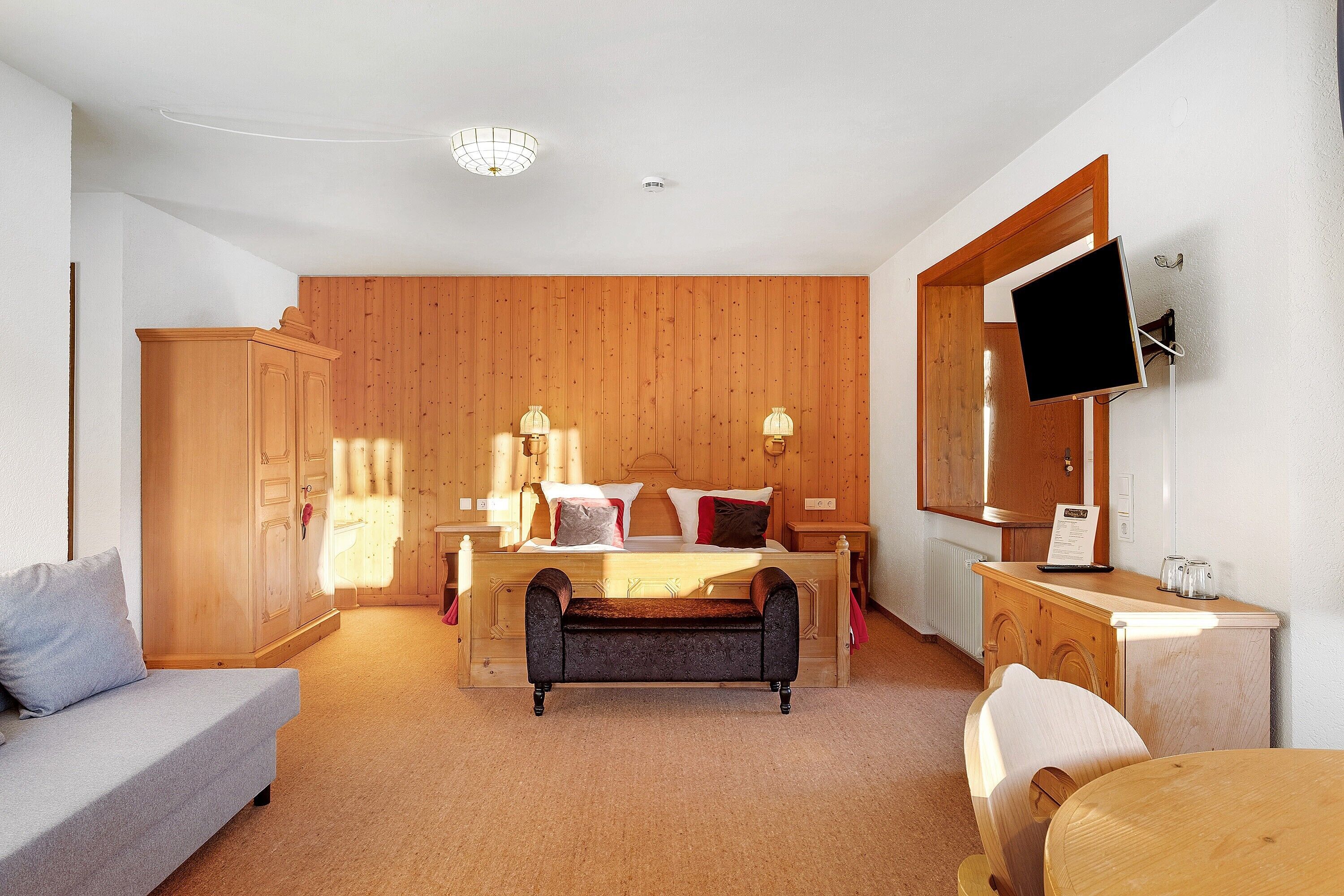 A bedroom with a bed, bedside tables, a TV, a wardrobe, and a bench.