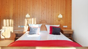 Ein Schlafzimmer mit einem hölzernen Kopfteil, zwei Nachttischen mit Lampen, einem Bett mit weißer und roter Bettwäsche und einer Holzvertäfelung.