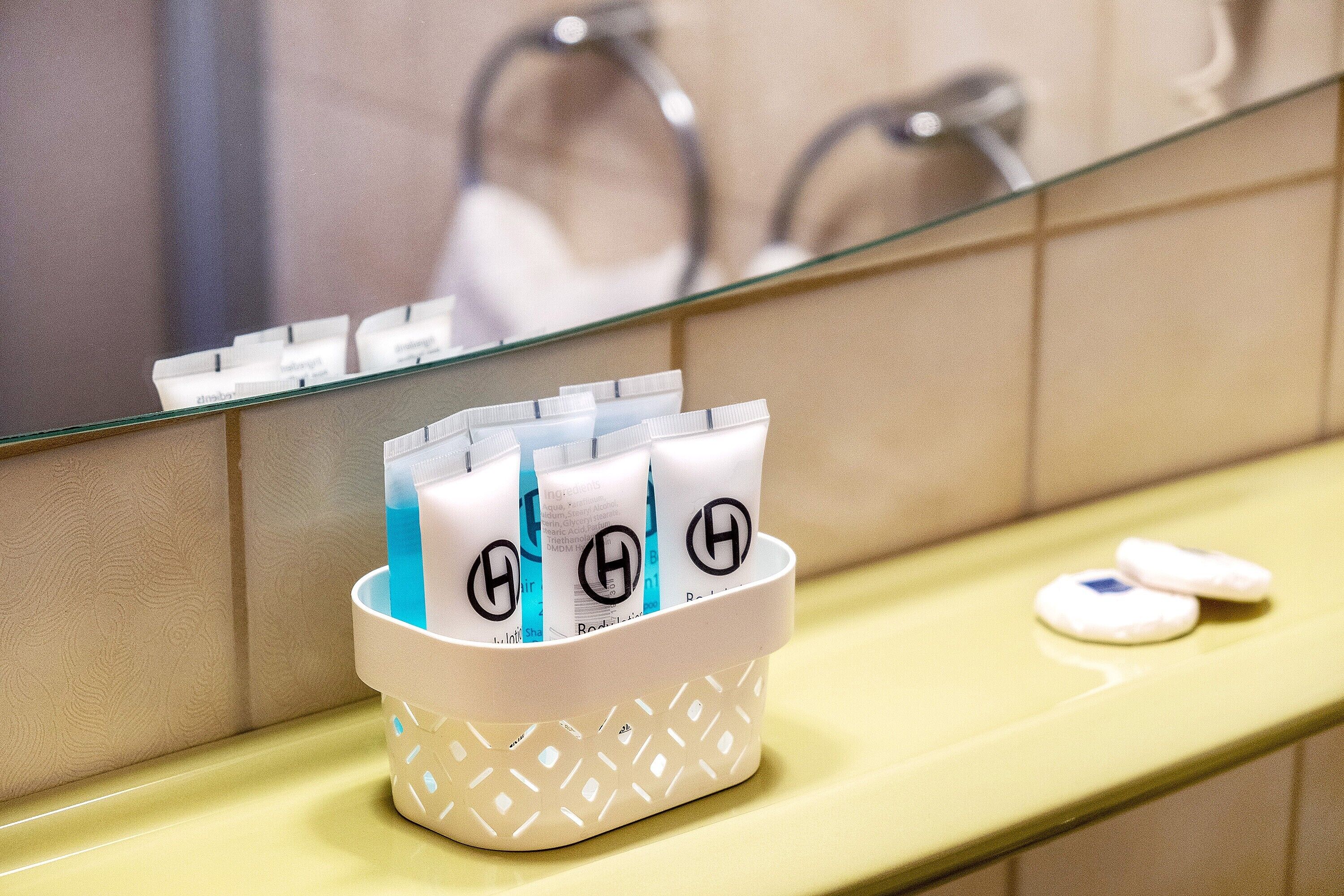 A bathroom with a mirror, a sink, and a basket containing toiletries.