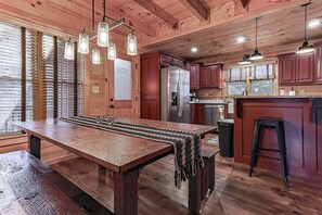 Una cocina de madera con una gran mesa de comedor, lámparas colgantes y un refrigerador.