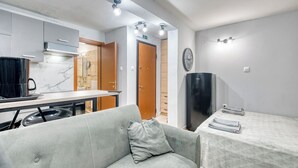 Un espacio habitable compacto con kitchenette, sofá, mesa de comedor y cama.