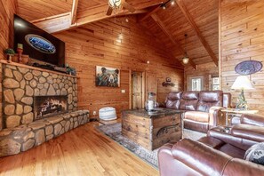 Ein Interieur einer Holzhütte mit Kamin aus Stein, Ledermöbeln, einem Fernseher und Holzwänden.