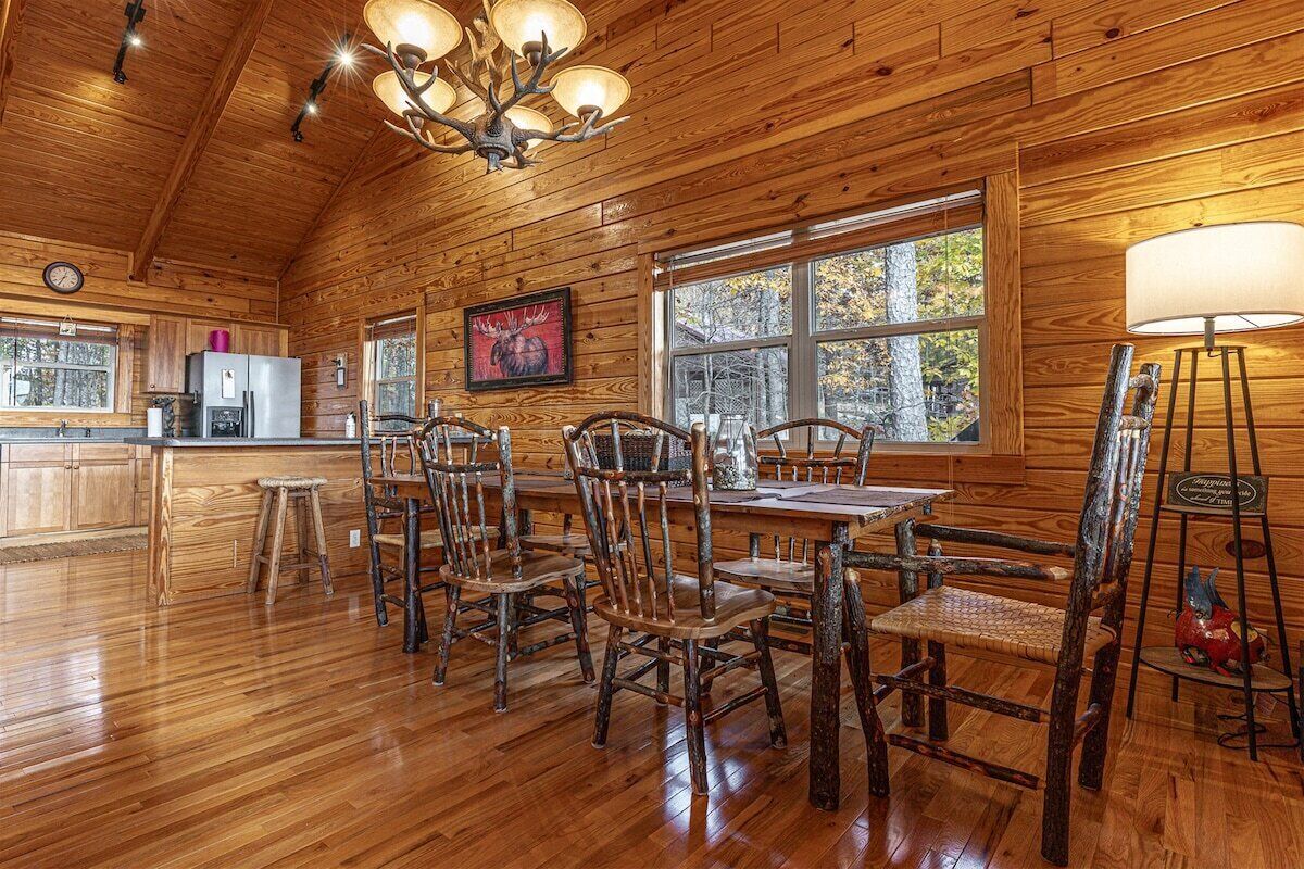 Un interior rústico de madera con una zona de comedor, techo de madera y ventanas grandes.