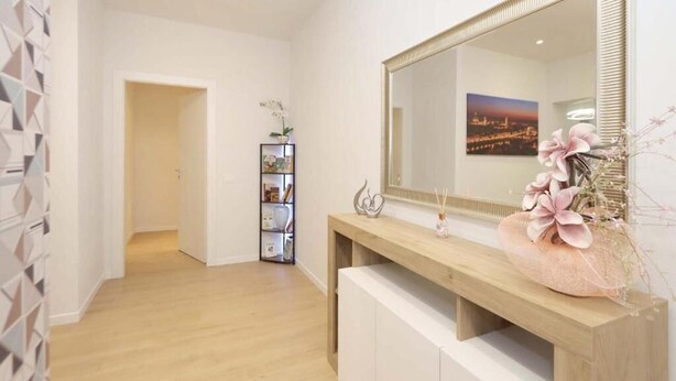 Un baño moderno con un espejo grande, tocador de madera y un jarrón decorativo con flores.