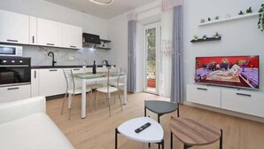 Una cocina moderna con armarios blancos, una mesa de comedor y sillas. Hay un televisor montado en la pared y un control remoto sobre una mesita.