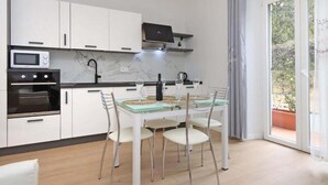 Una cocina moderna con armarios blancos, horno empotrado, microondas y un comedor con mesa y sillas de vidrio.