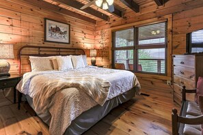 A wooden-paneled bedroom with a bed, a nightstand, a dresser, and a window with blinds. - Heavenly View Lodge | Ellijay, GA (Ellijay)