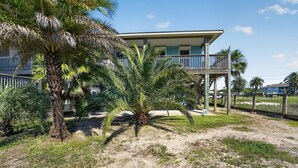 Een pand aan het strand met een gebouw van twee verdiepingen, een overdekt balkon en een palmboom.
