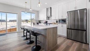 Une cuisine moderne avec des meubles blancs, un réfrigérateur en acier inoxydable et un grand îlot central doté de tabourets de bar.