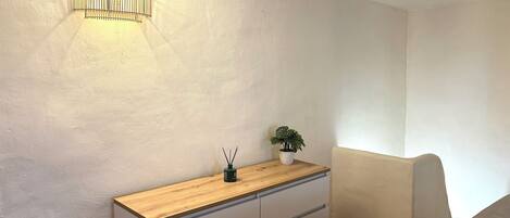 A room with a wooden dresser, a small potted plant, and a wall-mounted light fixture.