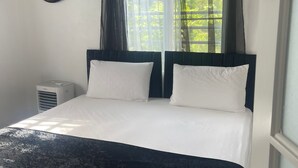 Een tweepersoonsbed met zwart-wit beddengoed, een klein airco-apparaat en een raam met dunne gordijnen.