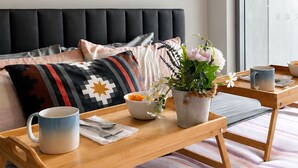 A modern bedroom with a bed, a bedside table with a mug, a bowl of fruit, and a potted plant.