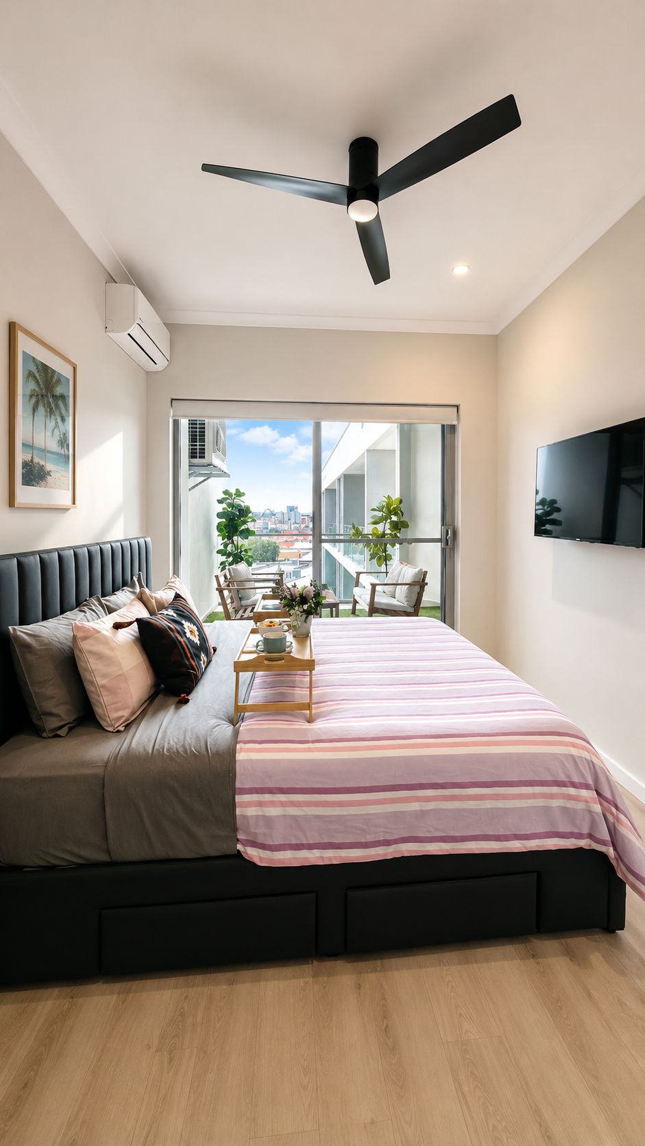 Une chambre moderne équipée d’un lit, d’un ventilateur de plafond, d’une télévision et d’un balcon offrant une vue sur la ville.