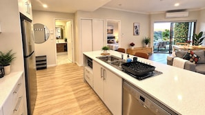 A modern kitchen with a dishwasher, a microwave, and a black grill. There is a dining area with a table and chairs. - Apartment with Balcony & Parking Perth (Perth)