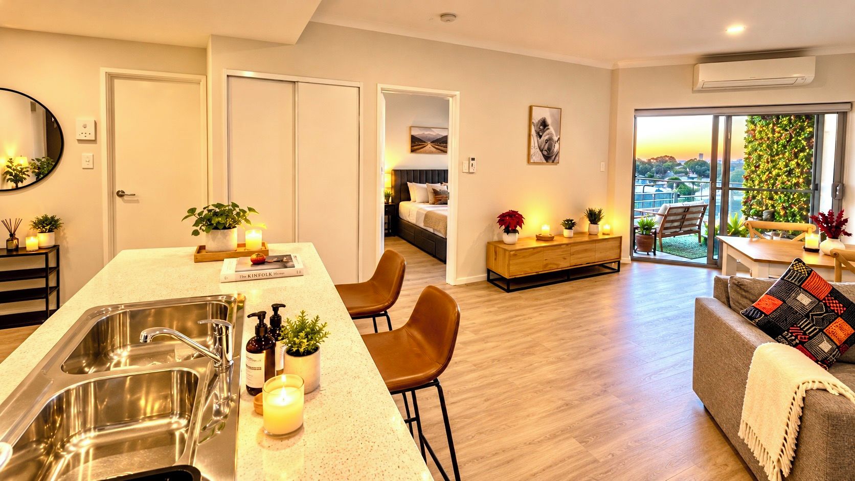 Una cocina moderna con una isla central, un comedor con sillas, un sofá y vistas a zonas verdes a través de grandes ventanales.