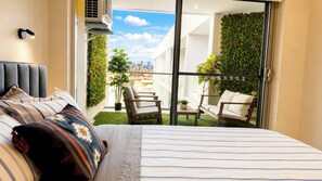 A hotel room with a bed, a view of the city, a balcony with plants, and a seating area. - Apartment with Balcony & Parking Perth (Perth)