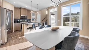 A modern kitchen with stainless steel appliances, a dining area with a large table and chairs, and a view of the outside through a sliding glass door. - Family-Friendly 3-Bed | Super Close to Airport! (Calgary)