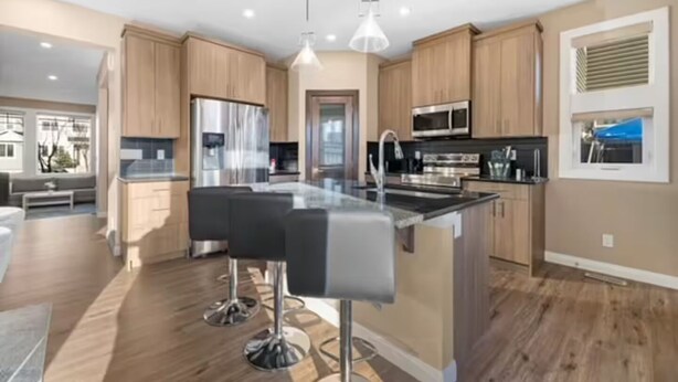 A modern kitchen with wooden cabinets, stainless steel appliances, and a central island with bar stools. - Family-Friendly 3-Bed | Super Close to Airport! (Calgary)